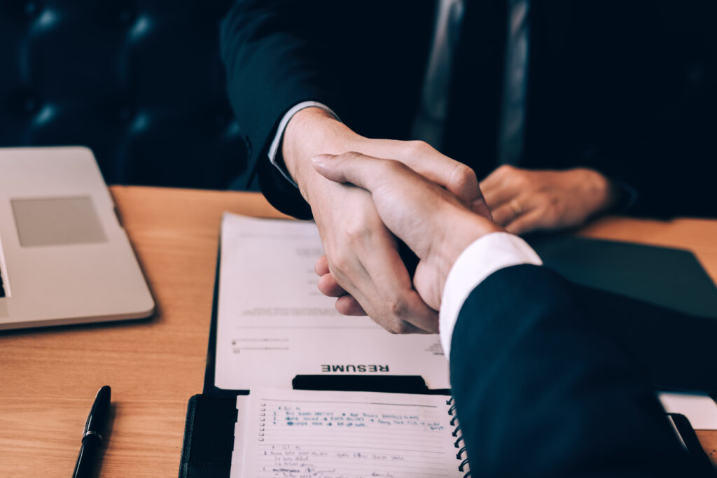 Two professionals shaking hands over a resume and notebook during a meeting to fulfill Singapore resident director requirements