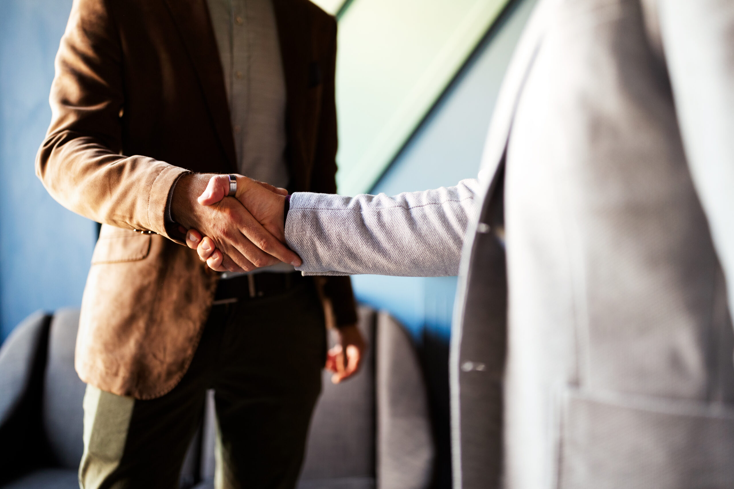 A close-up of two business professionals in blazers shaking hands in a modern office
