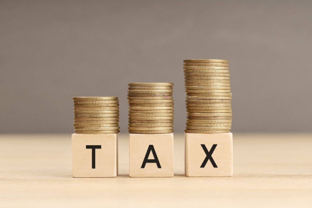 Increasing stacks of gold coins resting on three wooden blocks that spell T-A-X. The growing piles of coins represent the business savings achieved through the Start Up Tax Exemption Singapore
