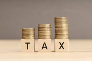 Increasing stacks of gold coins resting on three wooden blocks that spell T-A-X. The growing piles of coins represent the business savings achieved through the Start Up Tax Exemption Singapore