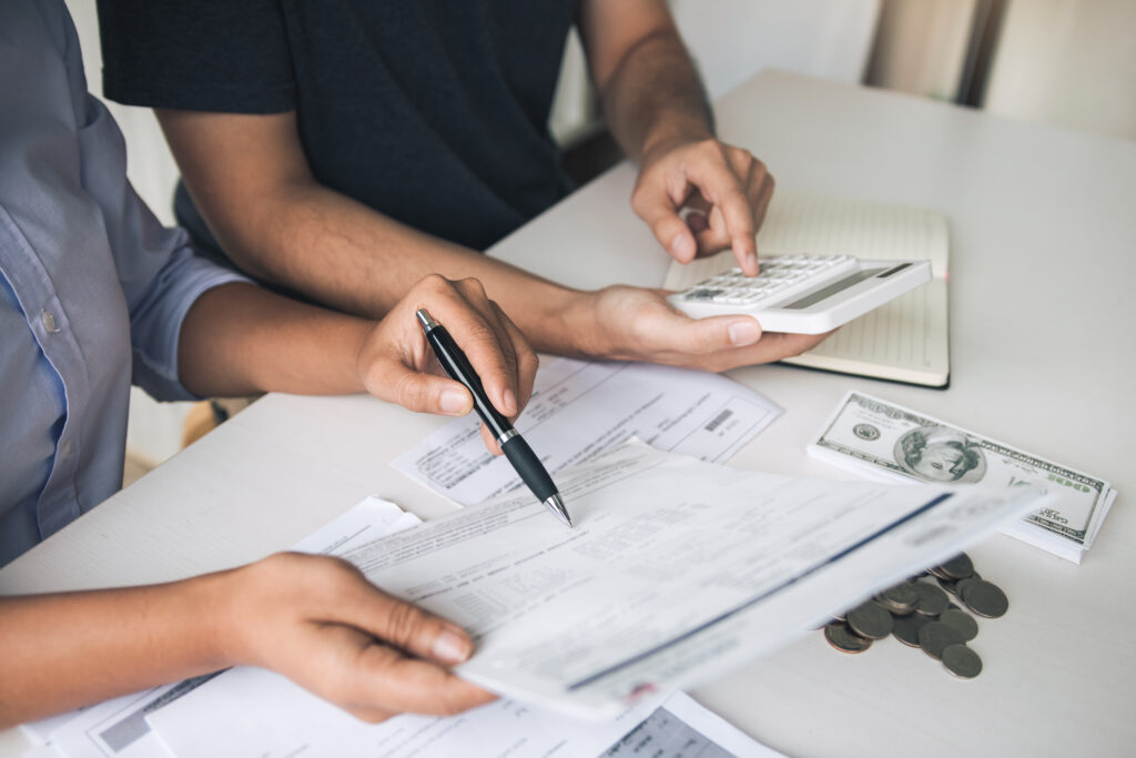 A couple sitting together at a table, using a calculator and checking their paperwork to get ready to file their estimated chargeable income in Singapore
