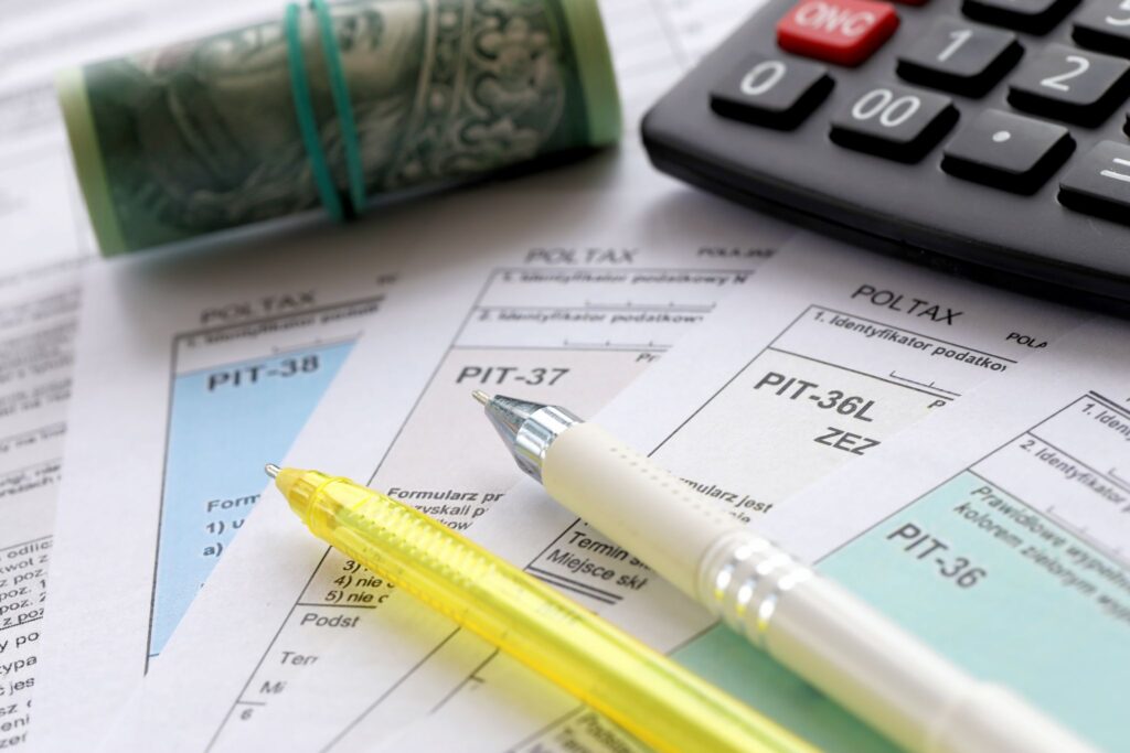 a stacks of paper with pens, a roll of cash, and a calculator