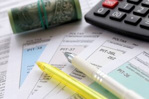 a stacks of paper with pens, a roll of cash, and a calculator