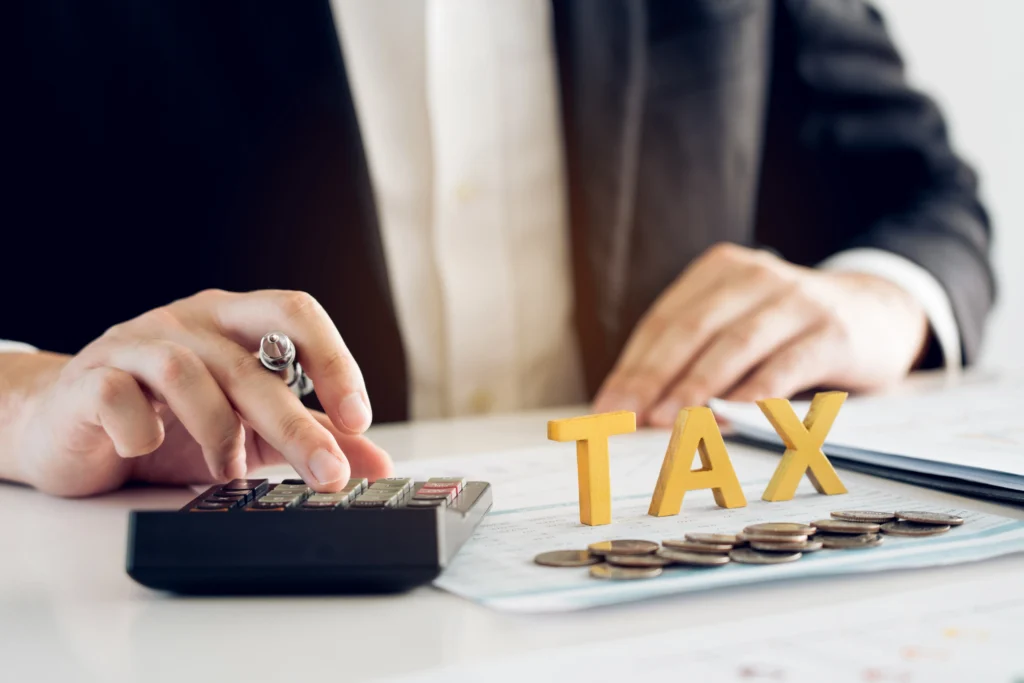 an accountant in a business suit working with a calculator, coins, and wooden letters spelling tax