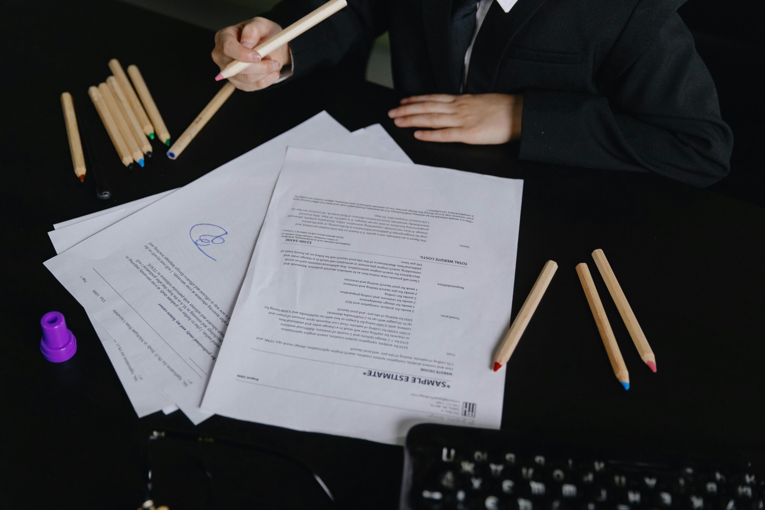 Person reviewing a printed sample estimate document at a desk with colored pencils and a keyboard