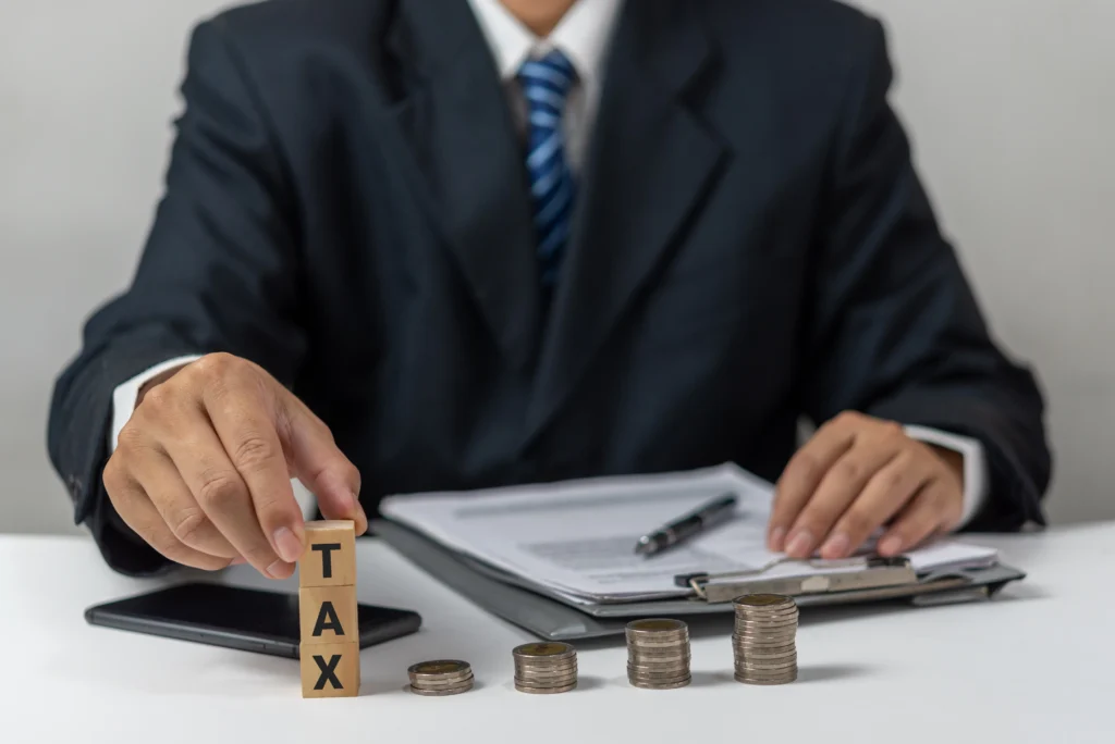 a businessman organizing wooden blocks spelling TAX next to stacked coins on an office desk